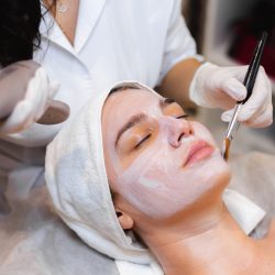 Beautician with a brush applies a white moisturizing mask to the face of a young girl client in a spa beauty salon Beautician with a brush applies a white moisturizing mask to the face of a young girl client in a spa beauty salon